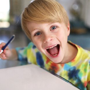 A very happy young boy drawing with a pen