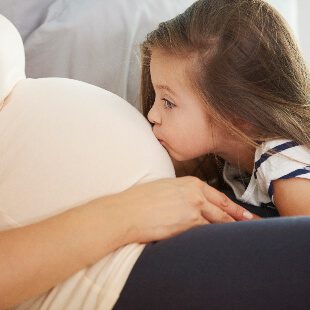 Young girl kissing mothers pregnant stomach