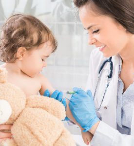 Smiling female doctor giving injection to infant with teddy bear