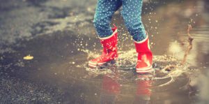 legs of child in red rubber boots jumping in the autumn puddles