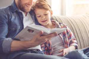Father and son are reading a book and smiling while spending time together at home